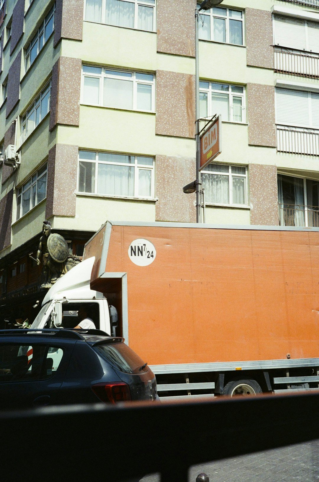 a-large-orange-truck-driving-down-a-street-next-to-tall-buildings-7hvxj1srxyk