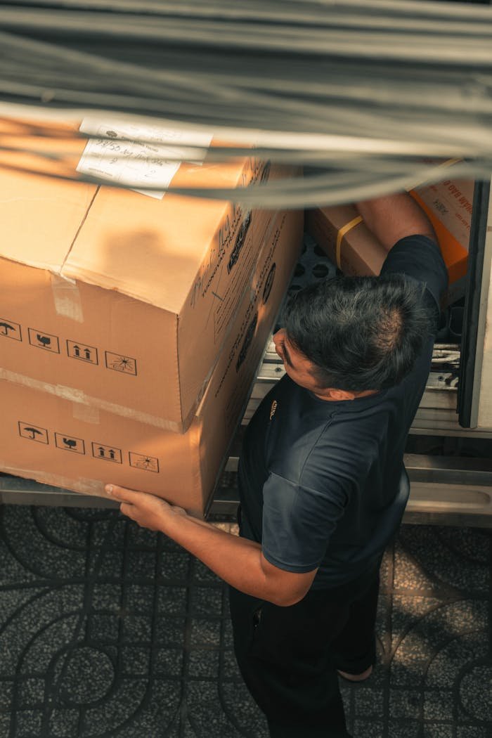 Delivery worker loading boxes from truck on urban city street during daytime.